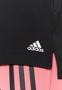Czarny sportowy top z białym logo Adidas po lewej stronie, zestawiony z różowo-czarnym paskowanym wzorem na dole. Gładki, elastyczny materiał.