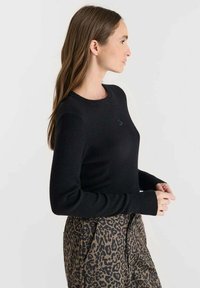 Pull noir à côtes avec des manches longues, présentant un col rond et un petit logo sur la poitrine. Assorti à un pantalon à imprimé léopard.