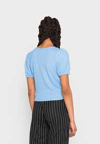 Hellblaues, geripptes Strickoberteil mit Puffärmeln und taillierter Taille, kombiniert mit schwarz-weißen gestreiften Hosen. Rückansicht gezeigt.