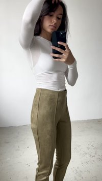 Top blanco de manga larga hecho de material translúcido combinado con pantalones ceñidos de ante sintético verde olivo que presentan costuras laterales y una textura suave.