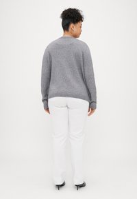 Harmaa neulepusero, jossa on pyöreä pääntie ja pitkät hihat, yhdistettynä valkoisiin housuihin. Materiaali näyttää pehmeältä, rennosti istuvalta ja ribbireunuksella varustetulta.