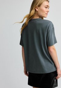 Graues Baumwoll-T-Shirt mit kurzen Ärmeln und lockerer Passform, mit einem Rundhalsausschnitt und glatter Textur, kombiniert mit einem schwarzen Lederrock.