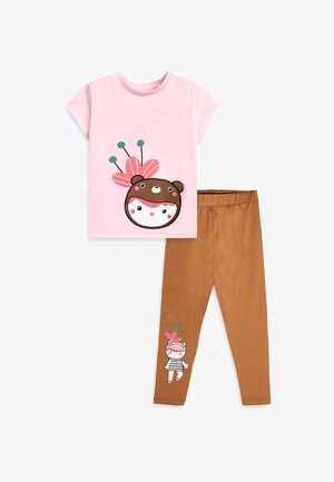 T-shirt rose à manches courtes avec un visage d'ours et un motif floral, associé à un legging marron présentant un petit personnage avec un chapeau fleuri près de l'ourlet.