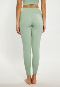 Zöld, magas derekú leggings sima textúrával és testhezálló fazonnal, széles derékpánttal és bokáig érő szabással.