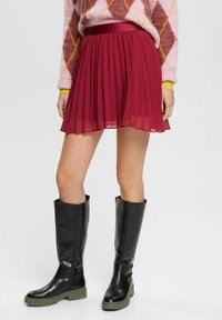 Bordeaux plisseret nederdel med en glat finish og en satin talje. Kombineret med stilige sorte knæhøje støvler med en robust sål.