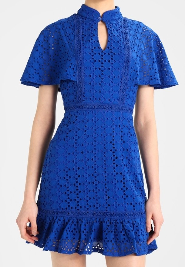 Vestido de encaje azul con un alto cuello, detalle de ojal, mangas cortas acampanadas y un dobladillo con volantes. Presenta patrones intrincados y una tela texturizada.