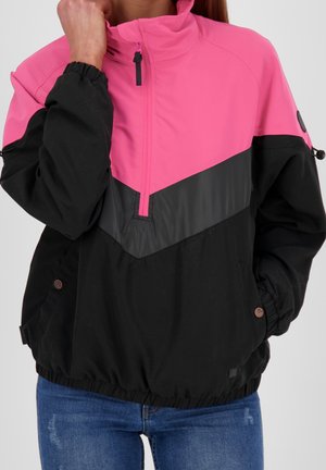 Femme portant une veste pull à blocs de couleurs rose et noire avec une fermeture éclair sur le devant jusqu'à mi-hauteur et des poignets élastiques, associée à un jean bleu.