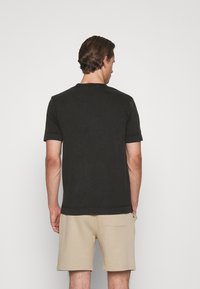 Zwarte T-shirt met korte mouwen en een ronde hals, gemaakt van zachte katoen. Draagt bij beige shorts met een achterzak.