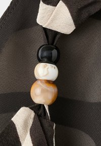 Trois perles rondes en noir, blanc et ambre sur un tissu rayé noir et blanc avec un détail froncé.