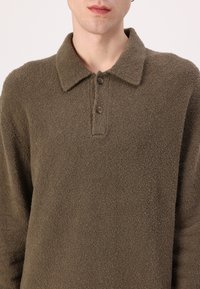 Brauner Fleece-Pullover mit Kragen, Zwei-Knopf-Leiste, weicher Textur und lässiger Passform. Verfügt über eine dezente, flauschige Oberfläche.