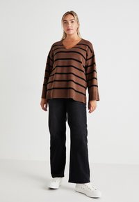 Pull marron rayé avec un col en V et des manches larges, associé à un jean large noir et des baskets blanches. Tenue simple et décontractée.