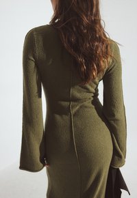 Olivovo zelené, textúrované šaty s dlhými, rozšírenými rukávmi a priliehavým strihom. Obsahujú stredný šev na chrbte a minimalistický dizajn.