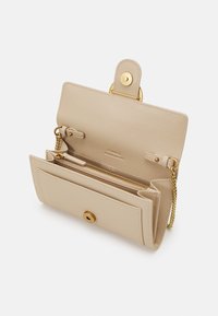 Carteira de couro bege com ferragens em tom dourado, apresentando uma alça de corrente, compartimento com fecho zipper e duas ranhuras para cartões no interior, com uma textura elegante e suave.
