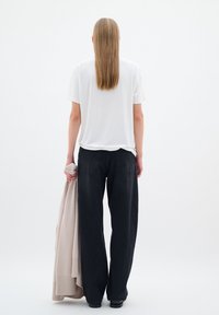 Camiseta blanca de manga corta, jeans negros de pierna ancha, sosteniendo un suéter de crema suave. El cabello lacio cae más allá de los hombros, estilo minimalista.