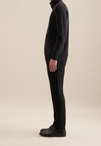 Tummanharmaa neulottu villapaita, jossa on korkea kaulus ja sivutasku, yhdistetty kapeisiin mustiin housuihin ja mustiin nauhakenkiin. Yksinkertainen, virtaviivainen muotoilu.