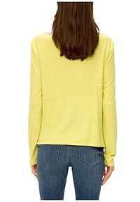 Lange mouwen, lichtgeel sweater met een ontspannen pasvorm, gemaakt van zachte stof; gecombineerd met blauwe spijkerbroek met een klassiek zakontwerp.
