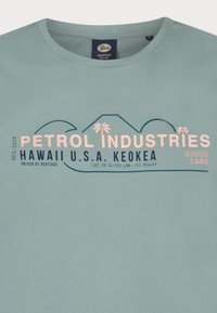 Světle modré bavlněné tričko s grafickým potiskem s textem "PETROL INDUSTRIES" a palmami, kulatým výstřihem a krátkými rukávy.