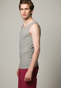 Hallika puuvillane tank top ribatud tekstuuriga, ümara kaelusega ja laia varrukakohaga, koos punaste lühikesed pükstega.