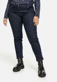 Tmavě modré džínové kalhoty s �úzkým střihem, které mají pět kapes, poutka na pásek a kontrastní šití. Doplněné o černé robustní boty.