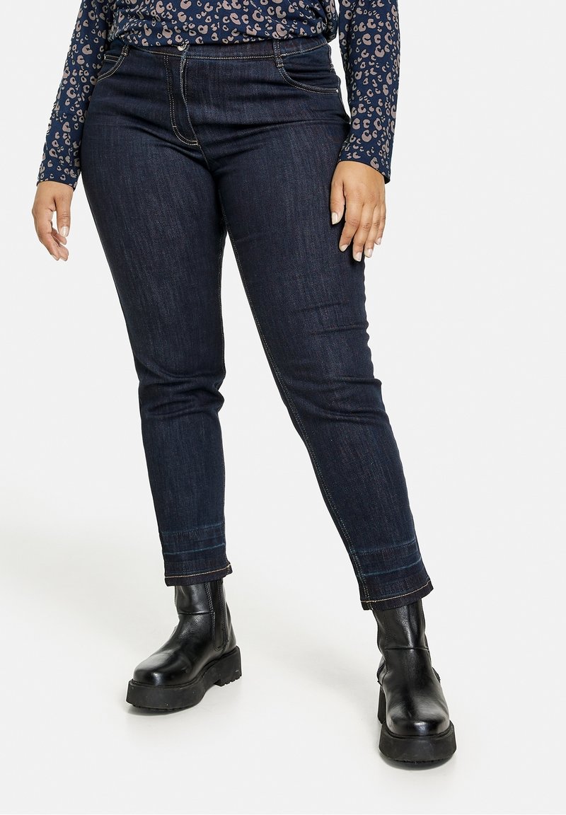 Tmavě modré džínové kalhoty s úzkým střihem, které mají pět kapes, poutka na pásek a kontrastní šití. Doplněné o černé robustní boty.