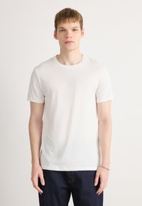 Kortermet, rundhalset t-skjorte i lys beige bomull, med et enkelt design uten mønstre, som står i kontrast til mørkeblå jeans.