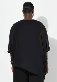 Túnica negra semitransparente con mangas cortas, dobladillo irregular y textura suave. Presenta un ligero drapeado y un minimalismo en los detalles en la parte trasera.