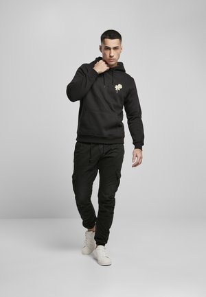 Black hoodie with a gold rose graphic, front kangaroo pocket, paired with black cargo pants and white sneakers. Plain background.