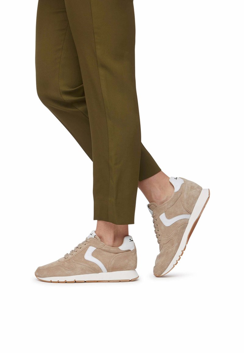Beige Wildlederschuhe mit weißen Akzenten und Gummisohlen, kombiniert mit olivgrünen Hosen, die ein schlankes, sportliches Design zeigen.