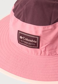 Καπέλο τύπου bucket με φαρδύ γείσο, ροζ και μοβ πάνελ, με ένα ορθογώνιο λογότυπο Columbia στο μπροστινό μέρος.