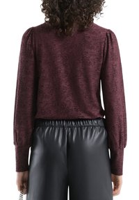 Teksturowany, bordowy top z długimi rękawami, z bufkami na ramionach. Połączony z czarnymi spodniami z imitacji skóry, podkreślającymi casualowy styl.