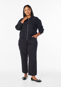 Černá bomber bunda s rozptýlenými jiskřivými detaily, se zipem, pružnými manžetami, spárovaná s černými kalhotami širokého střihu a lesklými černými balerínami se mašlí.