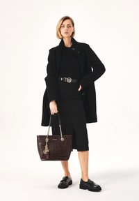 Palton negru din lână peste o rochie neagră ajustată, geantă de umăr maro închis cu model de crocodil și pantofi negri lucioși cu tălpi groase.
