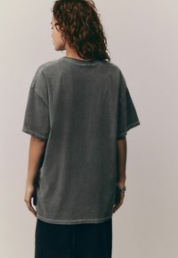 T-shirt en coton gris surdimensionné avec des manches courtes et un ourlet arrondi, présentant des coutures contrastées et une coupe décontractée.