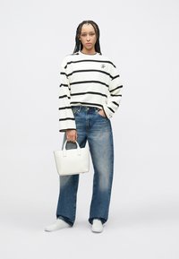 Weißes Langarmshirt mit schwarzen Streifen, blaue Jeans mit weitem Bein, weiße Sneakers und eine kleine weiße Handtasche. Einfaches und modernes Design.