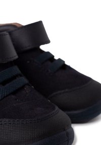 Zapatillas oscuras de color azul con una suela de goma texturizada, que cuentan con material de ante, correas de Velcro y cordones elásticos en contraste para un ajuste seguro.