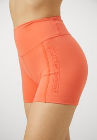 Shorts de sport Nike taille haute en corail avec une texture lisse, présentant un logo en relief et un lettrage de la marque sur le côté.