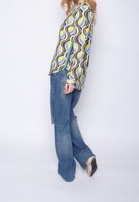 Pitkähihaine paita, jossa on monivärinen aalto-kuvio keltaisena, sinisenä ja ruskeana; yhdistetty kevyisiin sinisiin levennettyihin farkkuihin ja lenkkareihin.