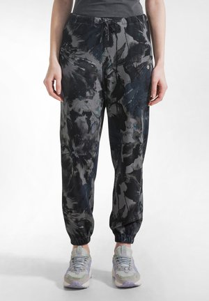 Zwartgrijze joggers met bloemenpatroon, een taille met trekkoord en elastische boorden, gemaakt van zacht stof. Gecombineerd met grijze sneakers.