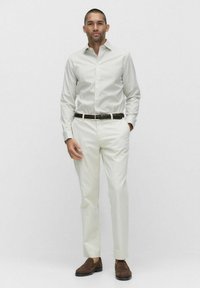 Wit gestreepte overhemde en crèmekleurige broek, bruine gevlochten riem en bruine schoenen. De outfit heeft een aansluitend ontwerp en een gladde textuur.