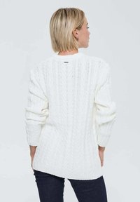 Pull en maille épaisse blanc avec une coupe décontractée, présentant des bords-côtes aux poignets et à l'ourlet. Longueur mi-longue à l'arrière avec une petite étiquette de marque au niveau du col.