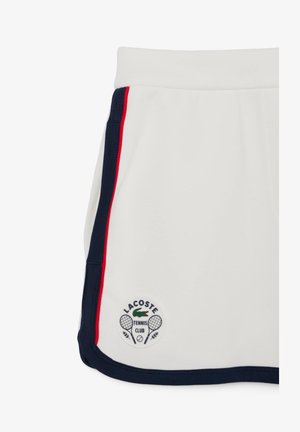 White tennis skirt with navy and red side stripes. Features a textured fabric and a round, embroidered logo at the hem.