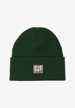 Zaļš adīts cepures modelis ar paceltu apkaklīti un taisnstūra plāksteri, kurā melnbaltā krāsā ir teksts "HOMEBOY loud-couture".