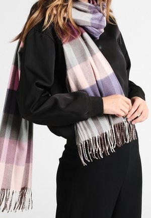 Écharpe à carreaux comportant des nuances de gris, rose et violet. Matière douce avec des bords frangés. Portée par-dessus un haut à manches longues de couleur foncée.