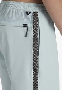 Shorts de sport bleu clair avec une taille élastique, une poche zippée sur le côté et un accent en motif zigzag noir sur le côté.