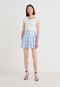 Gonna a quadri blu chiaro con pieghe, realizzata in tessuto intrecciato, abbinata a una maglietta bianca attillata. La modella indossa sandali neri con lacci.