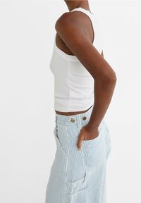 Top sin mangas blanco estriado combinado con pantalones de cintura alta a rayas azules y blancas que incluyen bolsillos y detalles metálicos. Vista lateral mostrada.