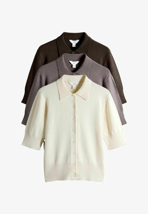 Tre korte, knapførte strikkede cardigans med kraver i creme, taupe og mørkebrun, lagdelt mod en hvid baggrund.