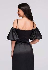 Robe en satin noir avec manches bouffantes épaules dénudées, corsage ajusté et silhouette droite. Dotée d'une fermeture éclair dans le dos.