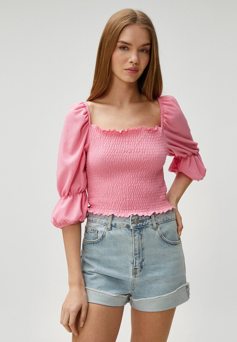 Lyserød smocket top med firkantet udskæring og korte puffærmer, parret med højtaljede denimshorts. Tekstileret stof og flæsekanter.