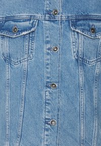 Chemise en denim bleu clair avec un devant à boutons classique, deux poches poitrine, des boutons-pression argentés et des détails de couture visibles.
